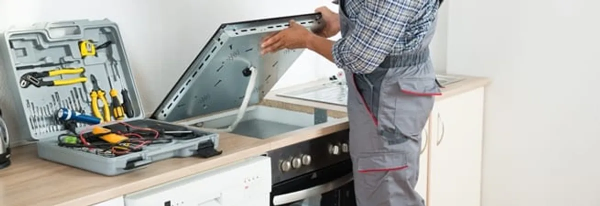 Cooktop repair technician lifting a built-in stovetop for service in Raleigh, NC